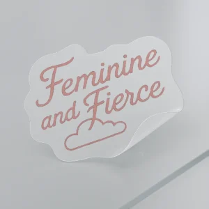 Wavy vinyl sticker with cursive pink text reading “Feminine and Fierce” above a small illustrated cloud. Features partial peel to showcase adhesive strength. Printed on clear vinyl with soft contour edging. Designed by PuffSticker.com as part of an empowerment-themed sticker collection for journals, laptops, and branding kits.