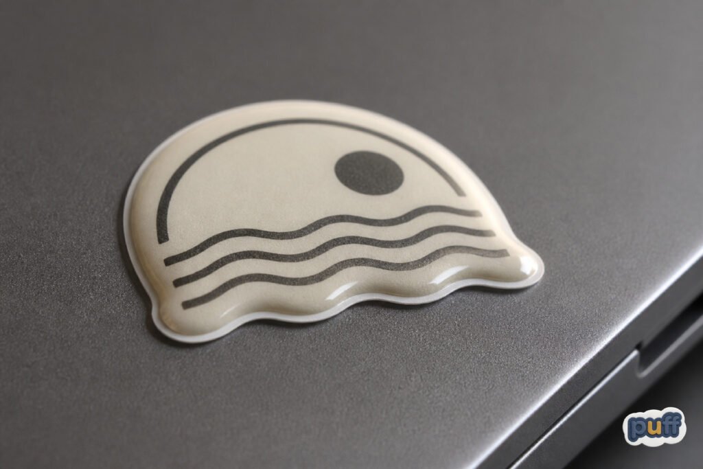 Why Some Custom Stickers Feel Like Objects 1 Macro photo of a custom dimensional sticker with a raised edge on a matte laptop lid, catching soft side light